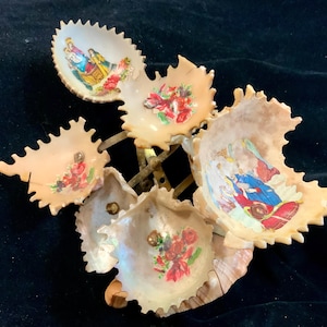 May include: A decorative serving dish with six leaf-shaped bowls. Each bowl is a light beige color and features a floral or religious image. The bowls are attached to a brass-colored metal frame.