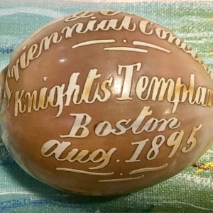 May include: A brown seashell with white lettering that reads "Triennial Conclave Knights Templars Boston Aug. 1895".