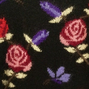 May include: Black knitted fabric with a floral pattern. The pattern features red, pink, and purple flowers with yellow stems and leaves.