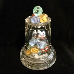 May include: A glass jar with a clear base and a glass lid filled with colorful marbles. The marbles are green, blue, red, and white.