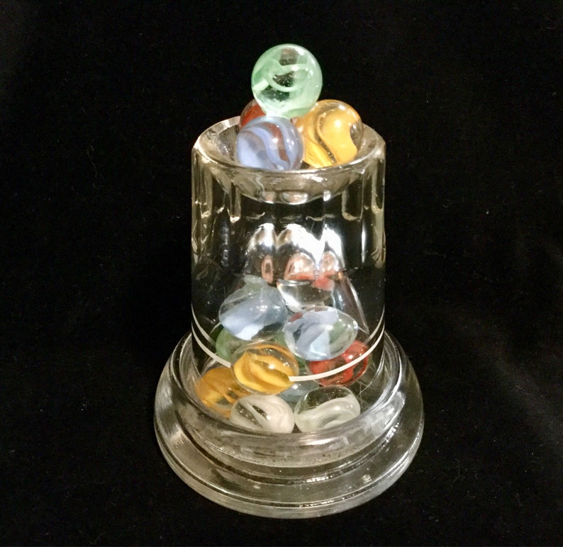 May include: A glass jar with a clear base and a glass lid filled with colorful marbles. The marbles are green, blue, red, and white.