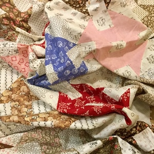 May include: A patchwork quilt made of various fabrics in shades of brown, pink, red, blue, and white. The quilt is made of squares and triangles, and the fabric patterns include floral prints, geometric designs, and polka dots.