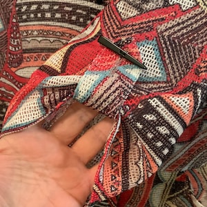 May include: A sheer, red, brown, and blue patterned top with a mesh design. The top has a geometric pattern and is made of a lightweight fabric.