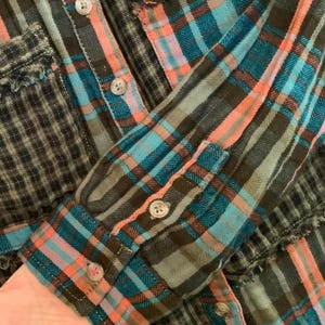 May include: A blue, pink, and brown plaid flannel shirt with frayed edges. The shirt has a button-up front and long sleeves.