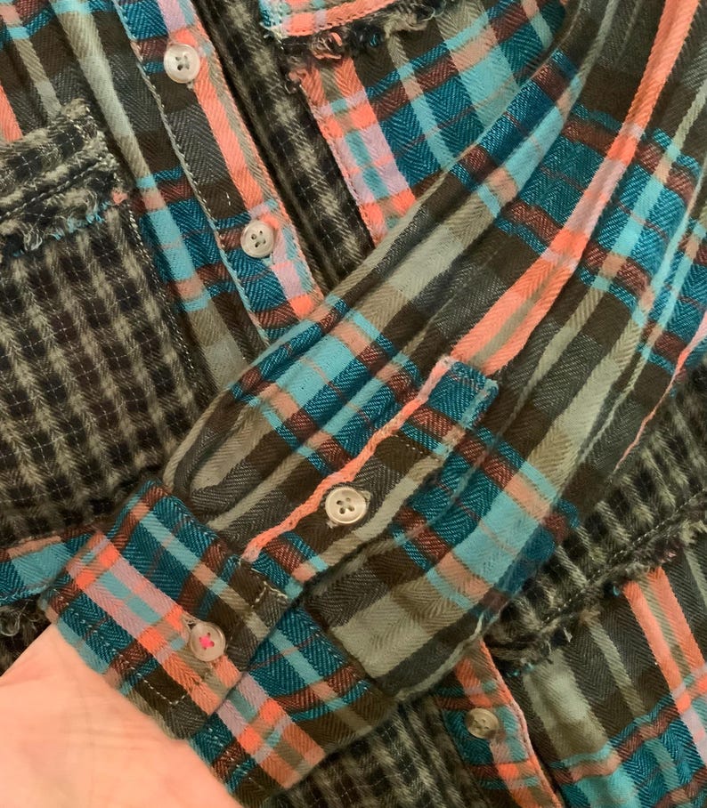 May include: A blue, pink, and brown plaid flannel shirt with frayed edges. The shirt has a button-up front and long sleeves.