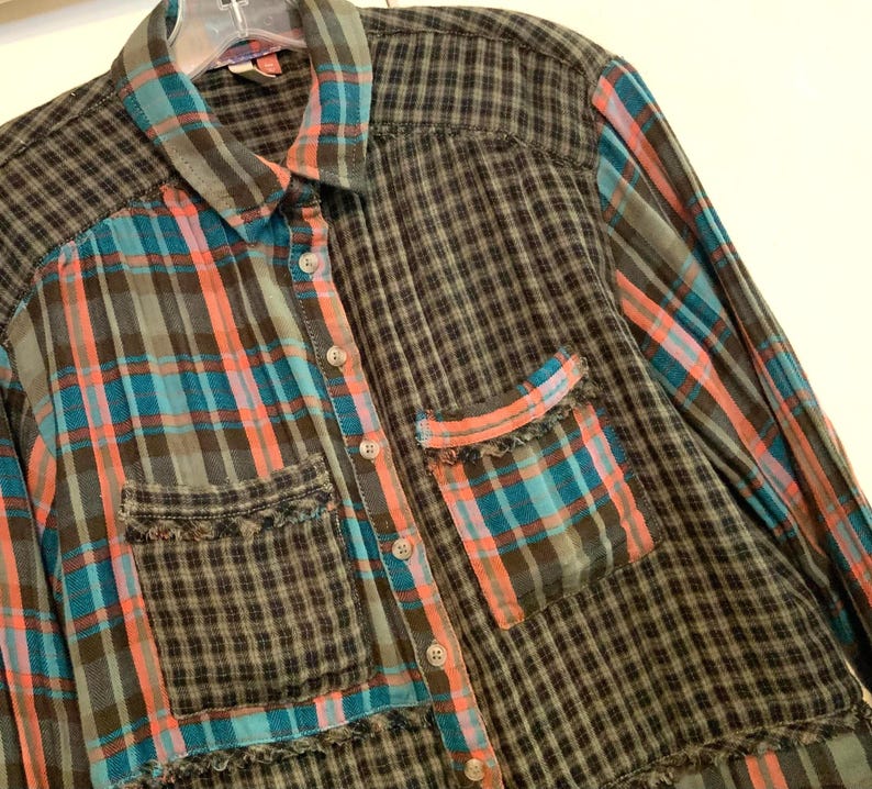 May include: A long-sleeved plaid shirt with a patchwork design in shades of black, blue, and pink. The shirt has a button-up front and a frayed hem.
