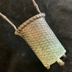 May include: A small, green, bronze, woven basket with two handles. The basket is made to look like a woven basket.