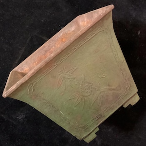 May include: A square green ceramic planter with a raised design of stylized flowers and leaves. The planter has four feet and a slightly raised rim.