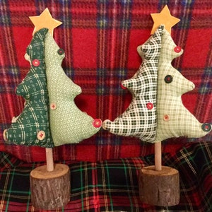 May include: Two handmade fabric Christmas trees with a plaid and green patterned design. The trees are standing on wooden bases and have a star on top.
