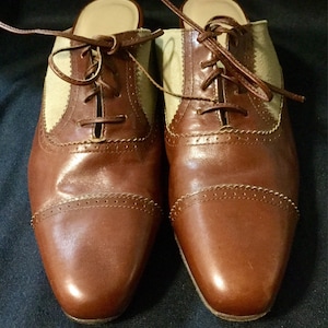 May include: A pair of brown leather heeled shoes with a beige canvas panel and lace-up closure.