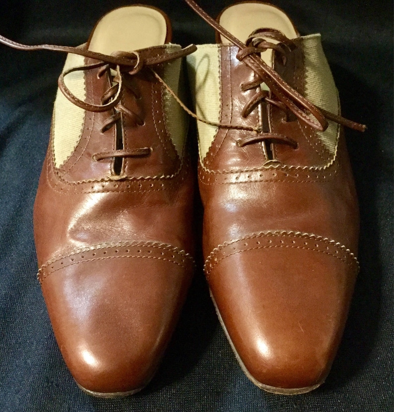 May include: A pair of brown leather heeled shoes with a beige canvas panel and lace-up closure.