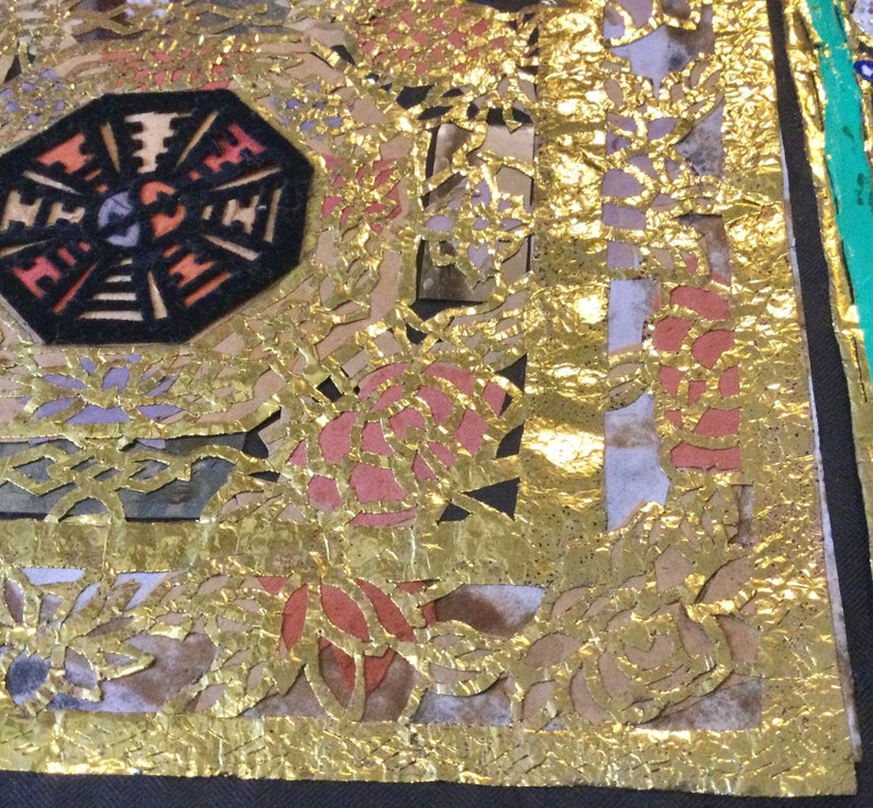 May include: A close-up of a fabric with a gold leaf design. The fabric has a geometric pattern with a black center and red and orange accents. The gold leaf is applied in a layered pattern, creating a textured effect.