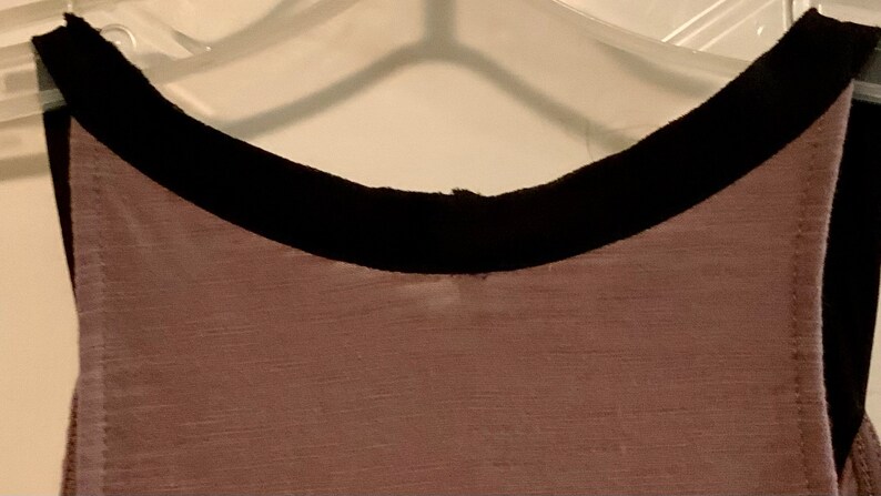 May include: A sleeveless top with a black trim around the neckline. The top is made of a soft, textured fabric.