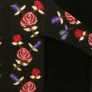 May include: Black cardigan sweater with a floral pattern of pink, red, and purple roses. The sweater has a button closure.