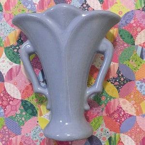 May include: A light blue ceramic vase with two handles. The vase has a fluted design and a rounded base.