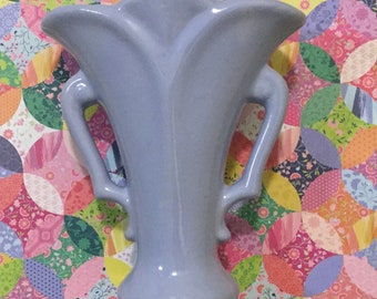 May include: A light blue ceramic vase with two handles. The vase has a fluted design and a rounded base.