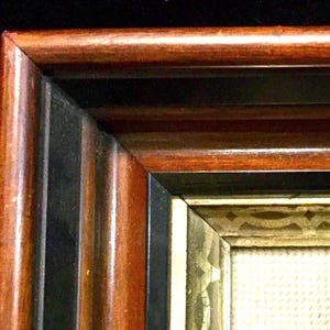 May include: Close-up of a wooden picture frame with a black and gold inner border. The frame has a rich mahogany color and a classic design.