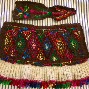 K&ouml;nnte beinhalten: Ein braunes Wollkleidungsst&uuml;ck mit einem bunten Stickmuster und einem wei&szlig;en gestrickten Fransenbesatz. Das Kleidungsst&uuml;ck hat ein separates St&uuml;ck braune Wolle mit Stickerei.