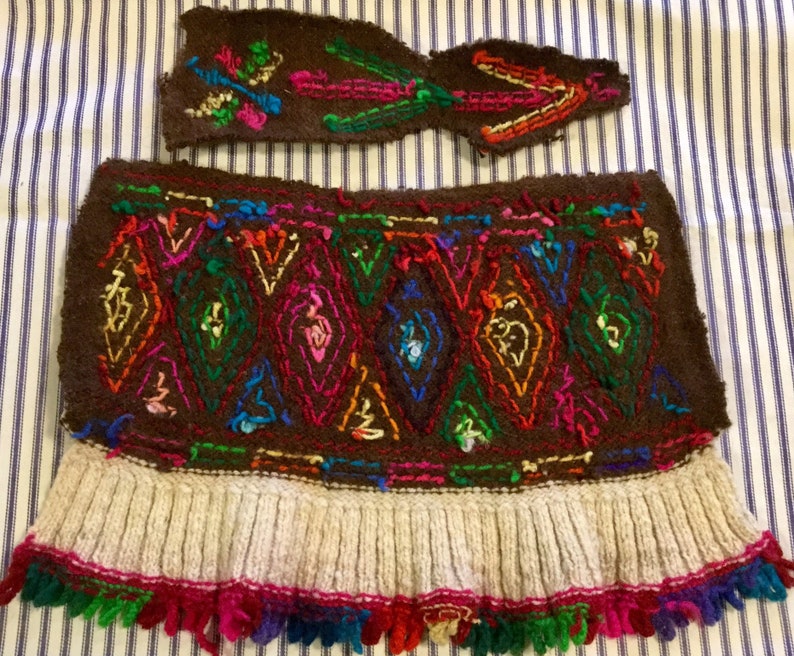 K&ouml;nnte beinhalten: Ein braunes Wollkleidungsst&uuml;ck mit einem bunten Stickmuster und einem wei&szlig;en gestrickten Fransenbesatz. Das Kleidungsst&uuml;ck hat ein separates St&uuml;ck braune Wolle mit Stickerei.