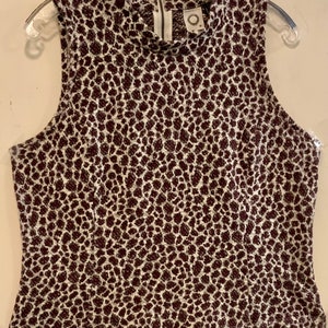 Puede incluir: Una blusa sin mangas de estampado de leopardo blanco y marr&oacute;n con cuello alto y cierre de cremallera en la espalda. La blusa tiene una peque&ntilde;a etiqueta redonda con el texto "Anthropologie" en la parte delantera.