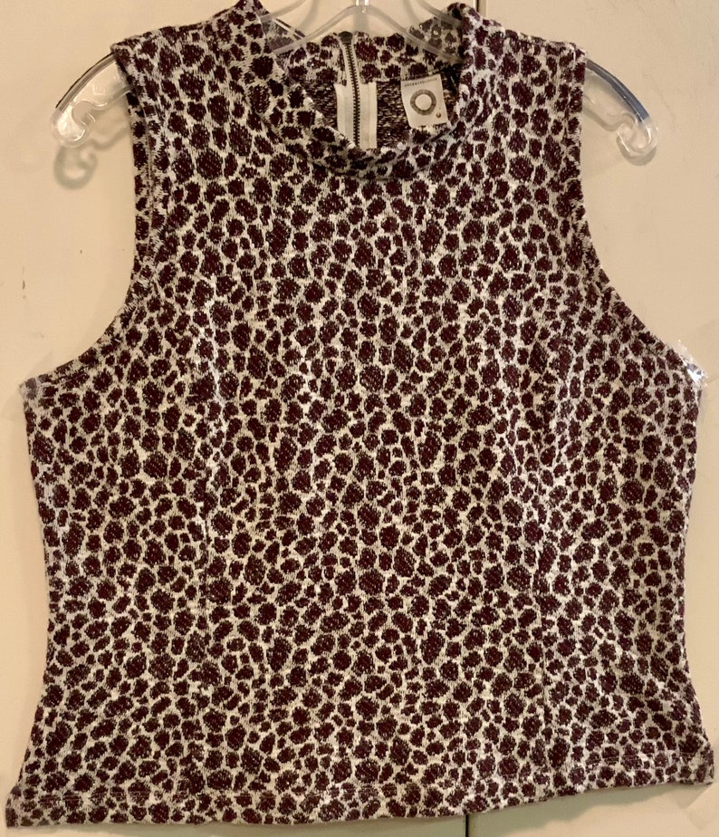 Puede incluir: Una blusa sin mangas de estampado de leopardo blanco y marr&oacute;n con cuello alto y cierre de cremallera en la espalda. La blusa tiene una peque&ntilde;a etiqueta redonda con el texto "Anthropologie" en la parte delantera.