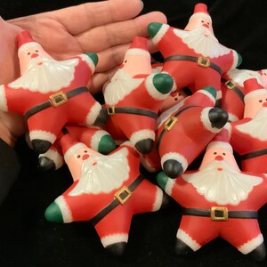 May include: A group of red and white star-shaped Christmas ornaments with a Santa Claus design. Each ornament has a green felt trim and a black belt with a gold buckle.