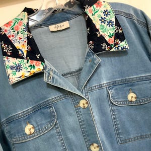 May include: A light blue denim shirt with a pointed collar featuring a dark navy blue floral pattern with pink, yellow, and blue flowers. The shirt has a button-down front, two chest pockets with button closures, and a label reading style & co.