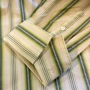 May include: A striped long-sleeve shirt with a button cuff. The shirt is made of a light-colored fabric with thin green and pink stripes.