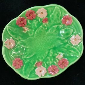 May include: A green ceramic dish with a raised floral design. The dish is decorated with pink and white flowers.