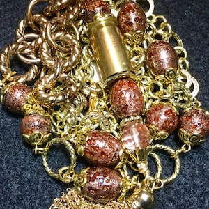 May include: A gold chain necklace with a brown and gold bullet charm, brown and gold beads, and a gold tassel.