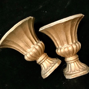 May include: Two gold-colored decorative urns with a fluted design. The urns are made of a textured material and have a classic, elegant style.