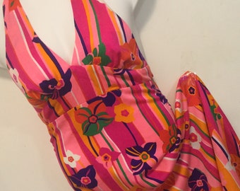 May include: A pink halter dress with a colorful floral and stripe pattern. The dress has a deep V-neckline and a fitted bodice.