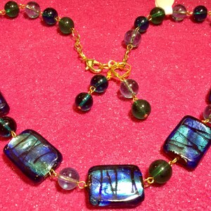 May include: A blue and green glass necklace with rectangular and round beads. The necklace is made with gold-toned metal connectors.
