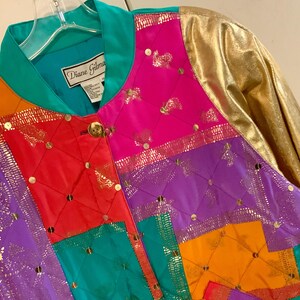 May include: A colorful quilted jacket with a gold metallic sleeve. The jacket is made of different fabrics in shades of teal, pink, purple, orange, and red. The jacket has a gold button closure and is decorated with gold sequins.