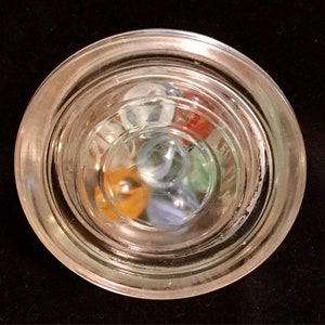 May include: A glass jar with a clear lid filled with colorful marbles. The marbles are blue, green, red, orange, and white.