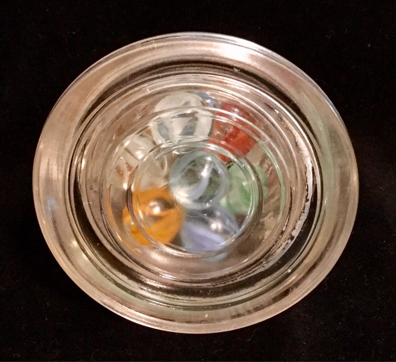 May include: A glass jar with a clear lid filled with colorful marbles. The marbles are blue, green, red, orange, and white.
