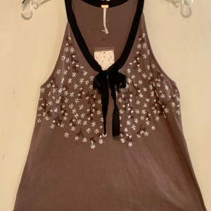 May include: A brown sleeveless top with a black trim and a bow at the neckline. The top is decorated with white embroidered flowers.
