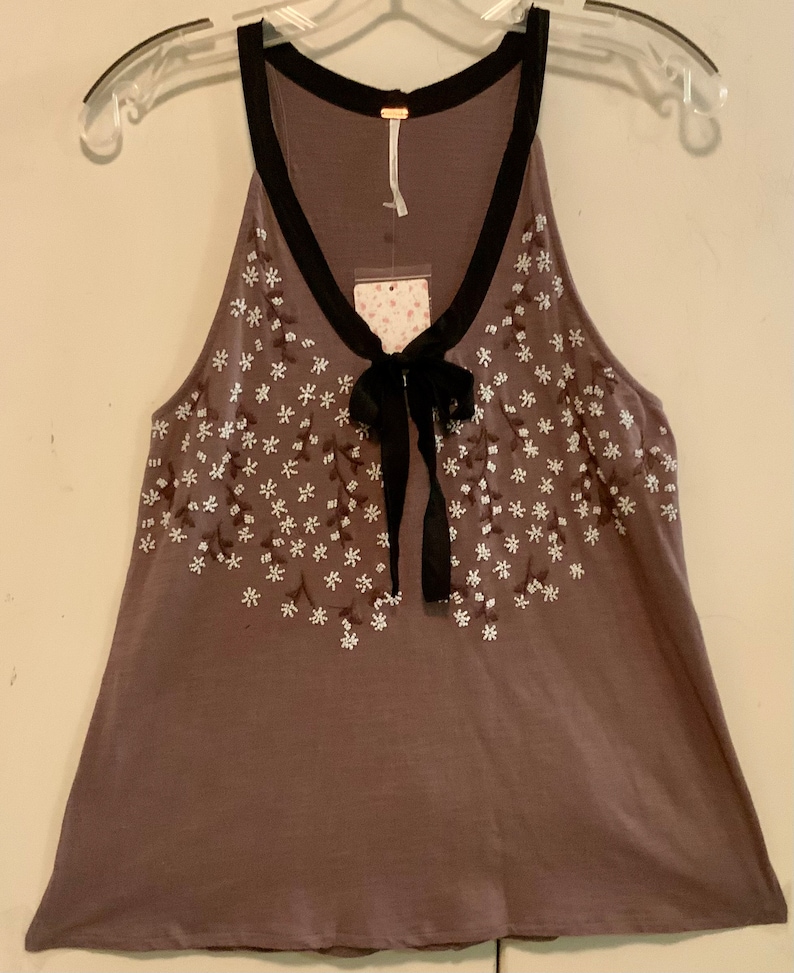 May include: A brown sleeveless top with a black trim and a bow at the neckline. The top is decorated with white embroidered flowers.