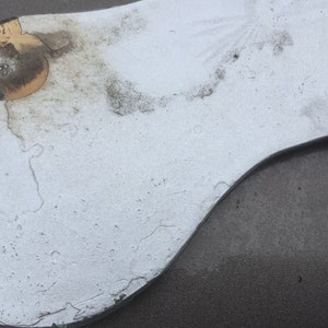 Pu&ograve; includere: Primo piano di una superficie bianca, usurata e leggermente danneggiata con una macchia marrone scuro. La superficie &egrave; curva e ha un bordo nero.