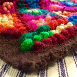 K&ouml;nnte beinhalten: Ein bunter Teppich mit braunem Fransenrand. Der Teppich ist aus Garn gefertigt und hat eine Vielzahl von Farben, darunter Rot, Gr&uuml;n, Blau, Gelb und Orange.