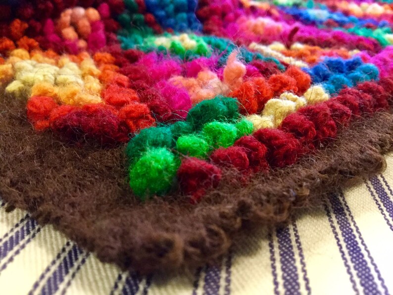 K&ouml;nnte beinhalten: Ein bunter Teppich mit braunem Fransenrand. Der Teppich ist aus Garn gefertigt und hat eine Vielzahl von Farben, darunter Rot, Gr&uuml;n, Blau, Gelb und Orange.