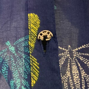 May include: Close-up of a navy blue fabric with a buttoned closure. The fabric has a pattern of white, yellow, and teal shapes. The button is silver and has a decorative design.
