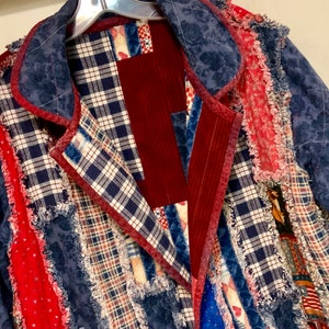 May include: A blue denim jacket with a patchwork design featuring red, white, and blue plaid fabric. The jacket has a frayed edge and a collar.
