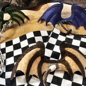 May include: Four pairs of felt dragon wings in different colors and patterns. The wings are attached to cords and are ready to be worn as a costume accessory.