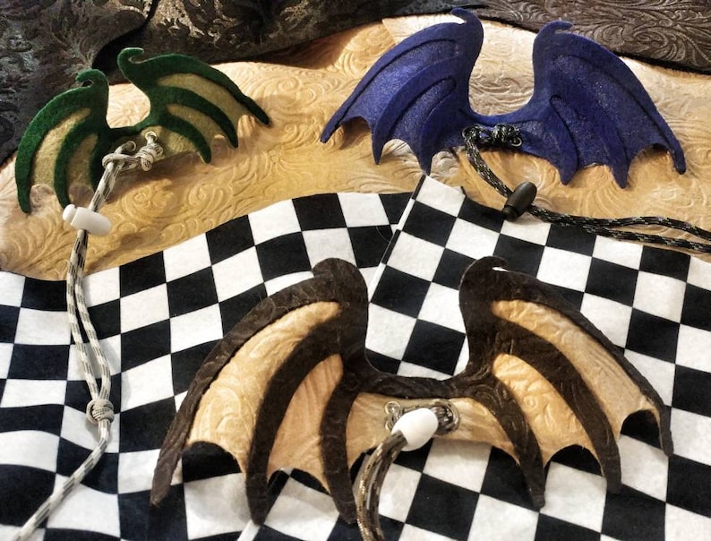 May include: Four pairs of felt dragon wings in different colors and patterns. The wings are attached to cords and are ready to be worn as a costume accessory.