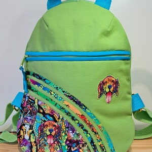 May include: A green canvas backpack with a blue zipper and a colourful dog print on the front. The backpack has a blue handle and adjustable straps.