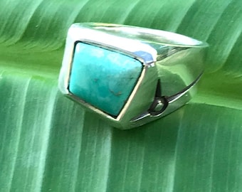 Puede incluir: Un anillo de plata con una piedra turquesa cuadrada engastada en el centro. El anillo tiene un diseño sencillo y está hecho de plata de ley.