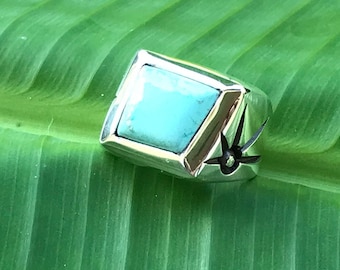 Puede incluir: Un anillo de plata con una piedra turquesa engastada en forma cuadrada. El anillo tiene un diseño de estrella en el lateral.