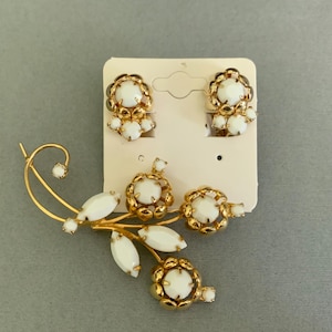 May include: A vintage jewelry set featuring a gold-tone brooch and matching clip-on earrings. The brooch is designed as a floral spray with white cabochon accents. The earrings and brooch have a gold-tone metal setting.