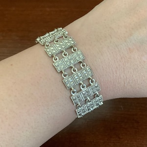 Può includere: Un braccialetto d'argento con un design geometrico. Il braccialetto è composto da più maglie rettangolari, ciascuna con una superficie testurizzata.